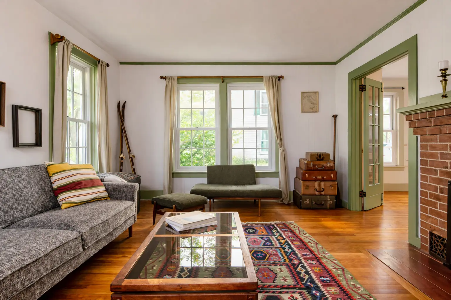 Light-filled farmhouse living room with green trim, vintage suitcases, and a patterned rug